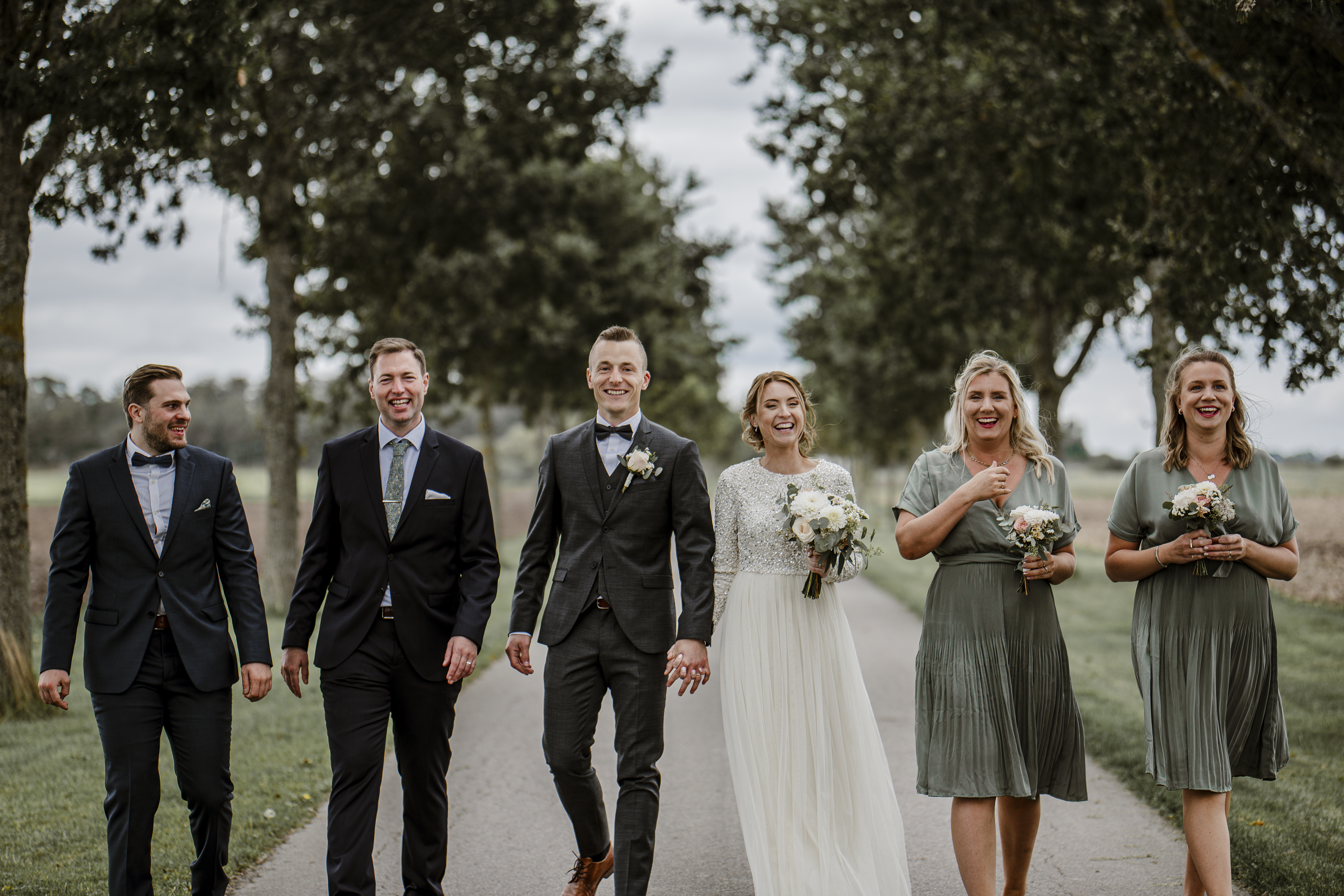 Brudpar med brudfölje under deras bröllopsfotografering på rosendals trädgård utanför stockholm