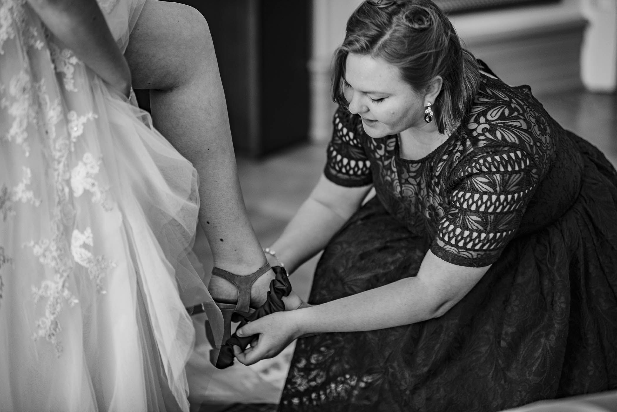 Dokumentär bild av brudens bästa vän som hjälper henne på med skorna